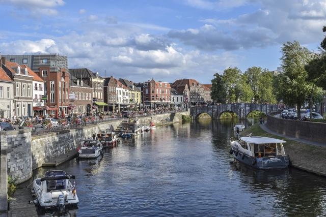 Zicht op het oude centrum van Roermond. We zien links een boulevard met historische panden, in het midden water met bootjes en rechts een oude brug die over het water loopt.