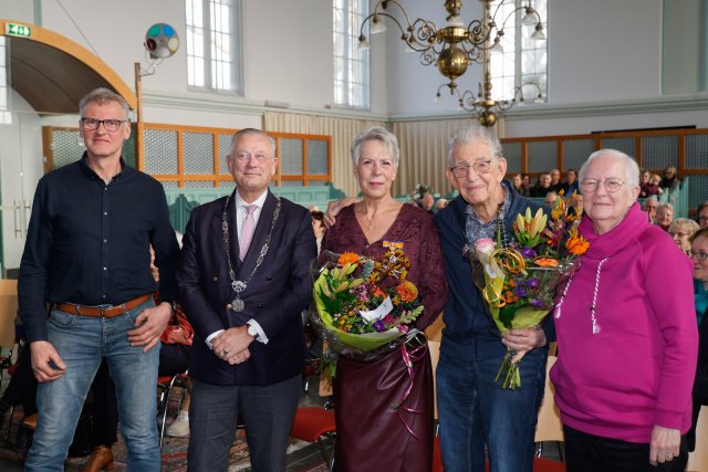 Burgemeester met ambtsketen twee gehuldigden met bloemen en familie