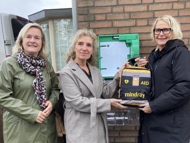 Wethouder Marian van Kampen en initiatiefnemers Nicole Kenter en Monique Kenter bij de officiële onthulling van de AED in Ursem.