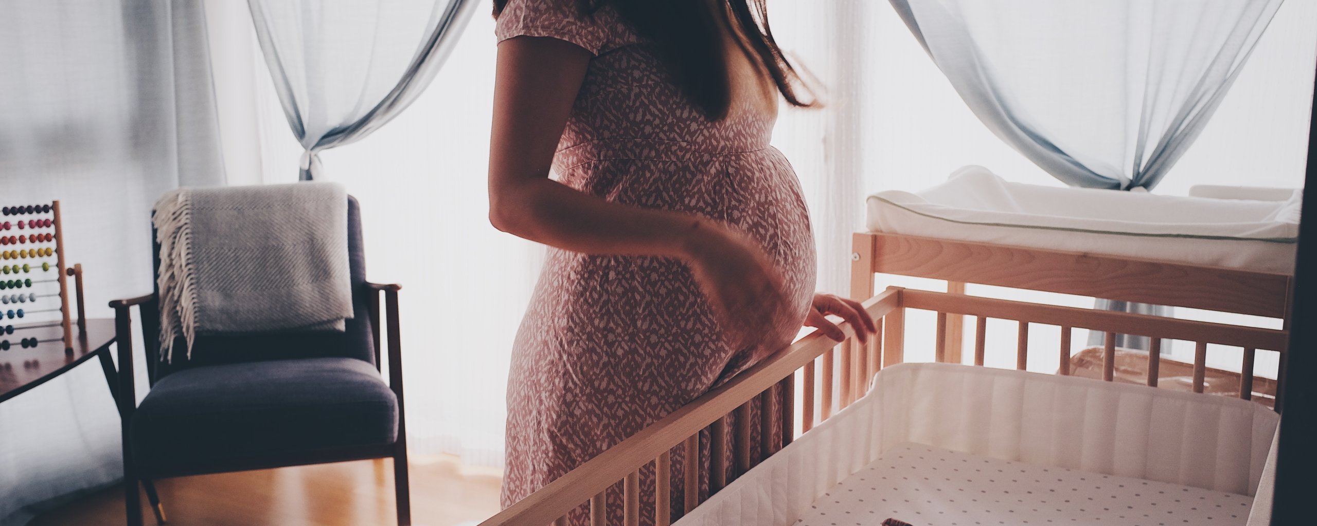 Zwangere vrouw staat bij lege ledikant