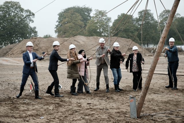 8 mensen die op een bouwterrein staan en een touw in hun handen hebben