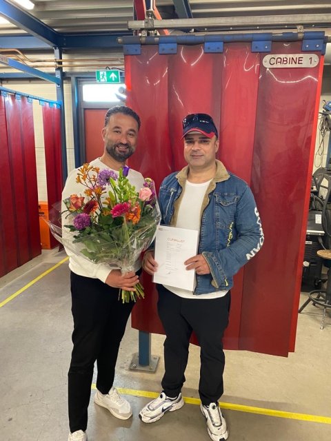 Twee mannen, 1 met een bos bloemen in zijn hand, de ander met een certificaat