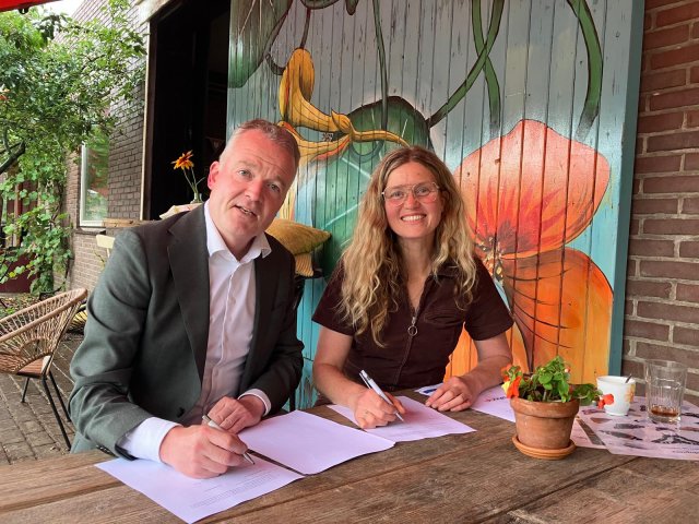 Een man en een vrouw zitten aan een tafel en hebben een pen in hun hand. Op tafell liggen papieren ter ondertekening