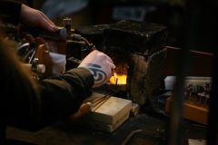 Een hand van een ambachtspersoon die met een gasbrander werkt bij een kleine oven of smeltkroes