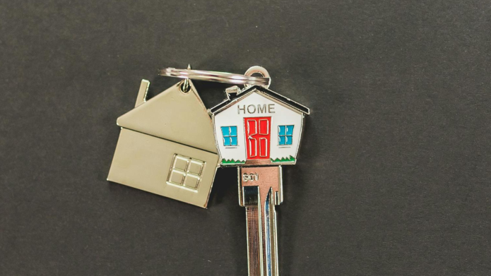 Huissleutel waarbij het uiteinde in de vorm van een gekleurd huisje is. Op het huisje staat de tekst home. Aan de sleutel hangt een metalen sleutelhanger in de vorm van een huis.