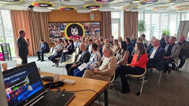 Mensen in Pinkpopzaal van het Burgerhoes die zitten te luisteren naar burgemeester Richard de Boer