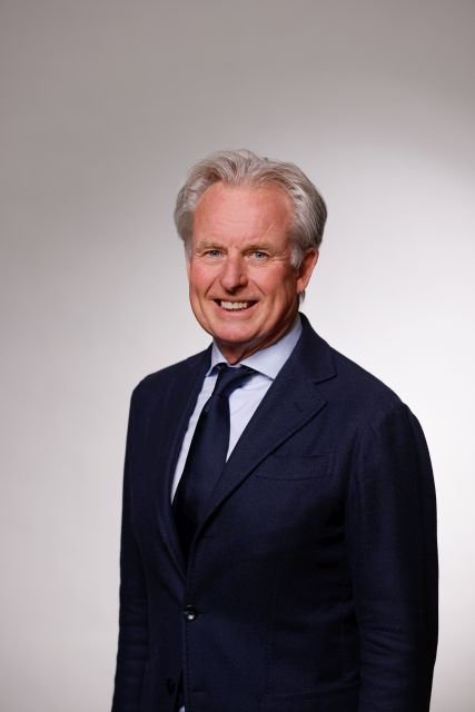 Persoon poseert in een donker maatpak voor een neutrale achtergrond