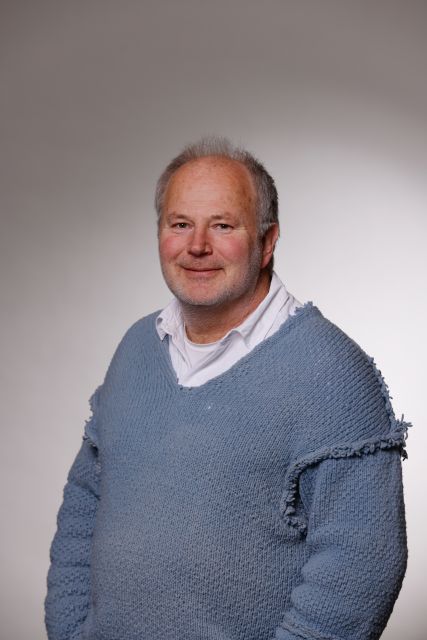 Persoon poseert in een lichtblauwe trui voor een neutrale achtergrond