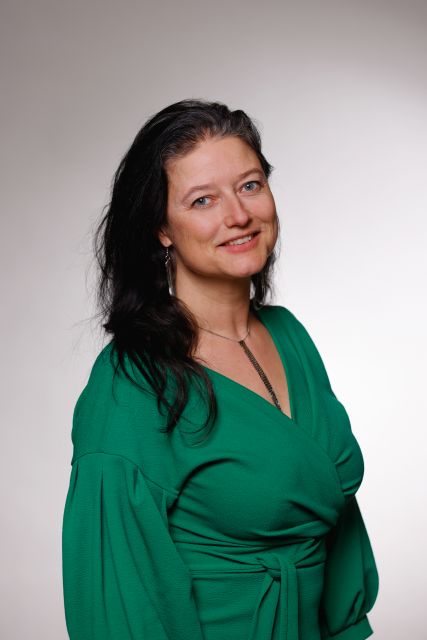 Persoon poseert in een groene jurk voor een neutrale achtergrond