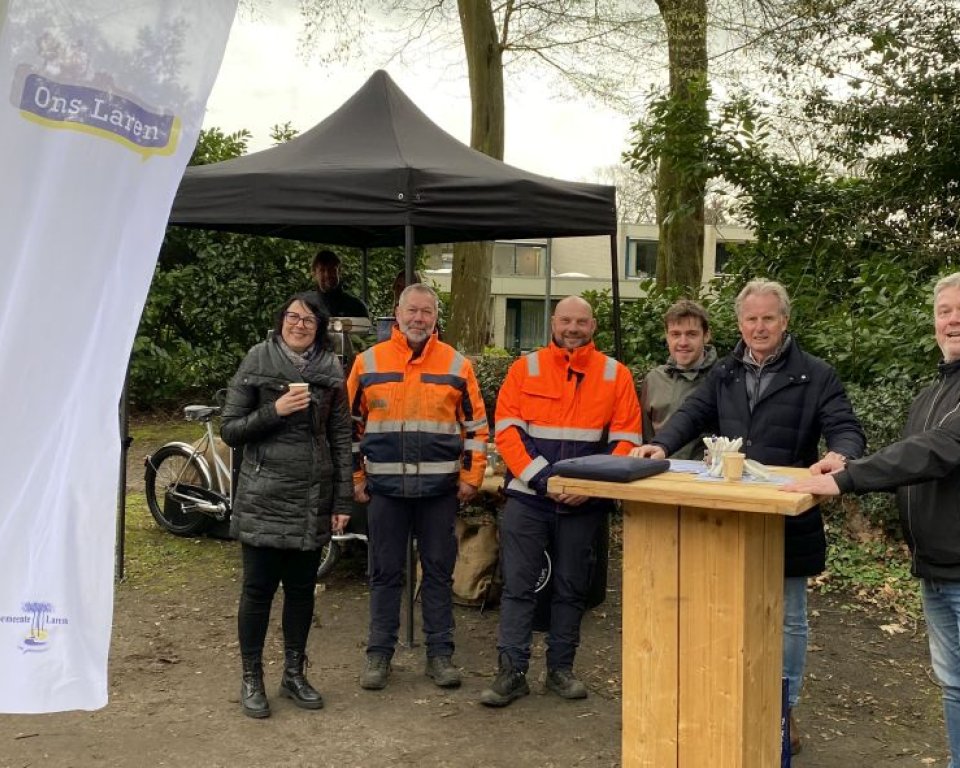 Groep mensen staat buiten bij een tent en houten tafel
