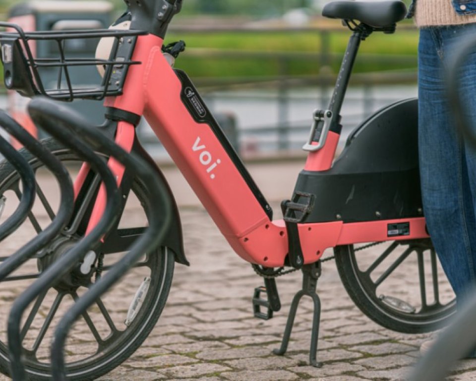 Persoon naast een rode deelfiets van Voi