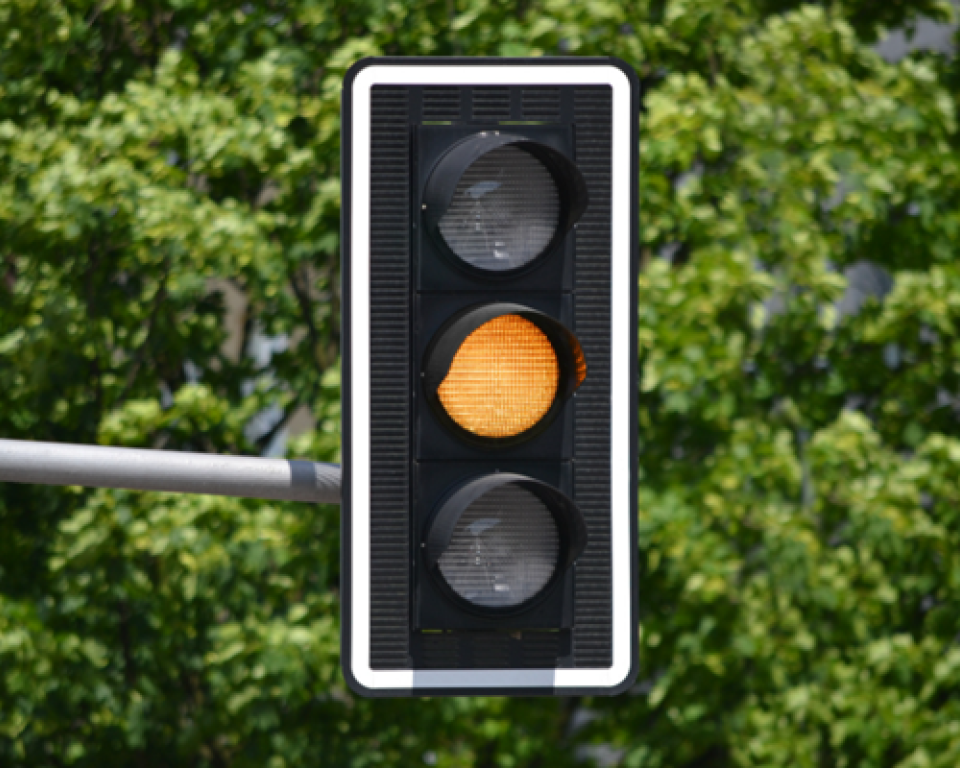 Verkeerslicht met oranje licht op een achtergrond van groene bomen.