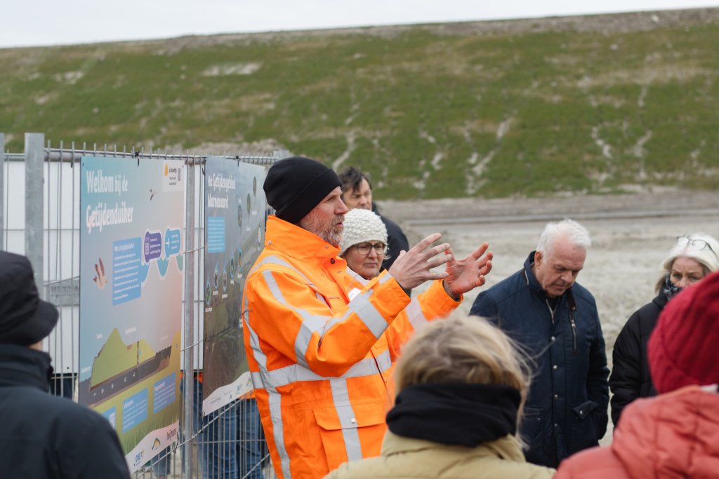 Het publiek loopt naar de getijdenduiker, achter de bouwhekken aan de binnenzijde op de nieuwe Lauwersmeerdijk. Hier worden ze aan de hand van een bordenserie meegenomen in de bouw, werking en het nut van de getijdenduiker.