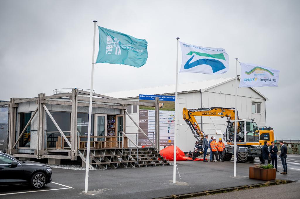 Het dijkinformatiecentrum en de schottenkeet met daarbij vlaggen van gemeente Het Hogeland, Waterschap Noorderzijlvest en Combinatie Waddenkwartier GMB Heijmans.