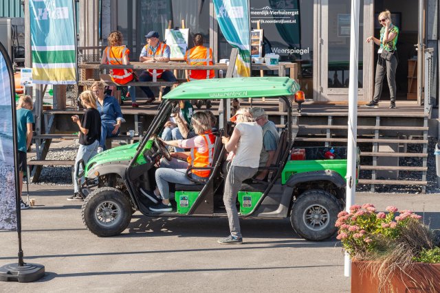 Een groen golfkarretje met bezoekers voor het dijkinformatiecentrum