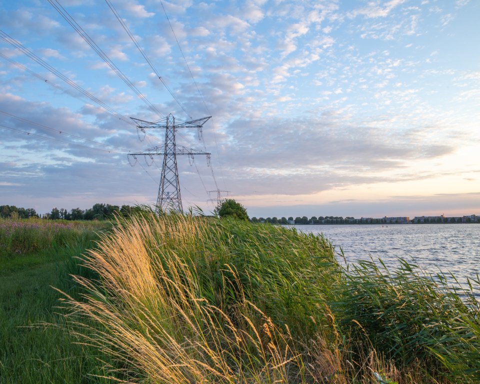 Elektriciteitsmast in een weiland met een watertje ernaast