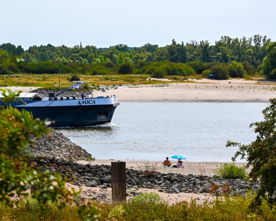 Waalstrand met vrachtschip en mensen op het strandje