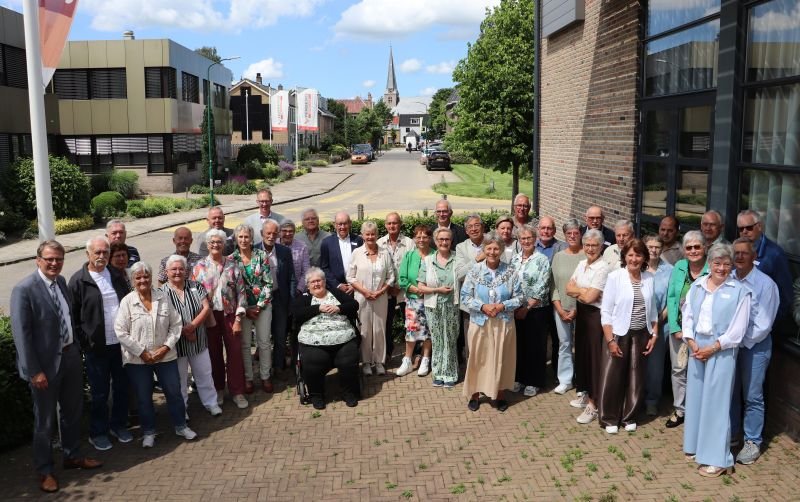 Groepsfoto van 18 jubilerende bruidsparen, burgemeester en wethouders buiten bij Dorpshuis XXL