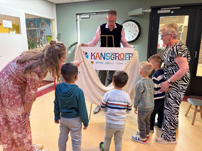 Wethouder Gerrit Spelt, vier kindjes van de Kansgroep en de twee leerkrachten onthullen het bord 'Kansgroep'