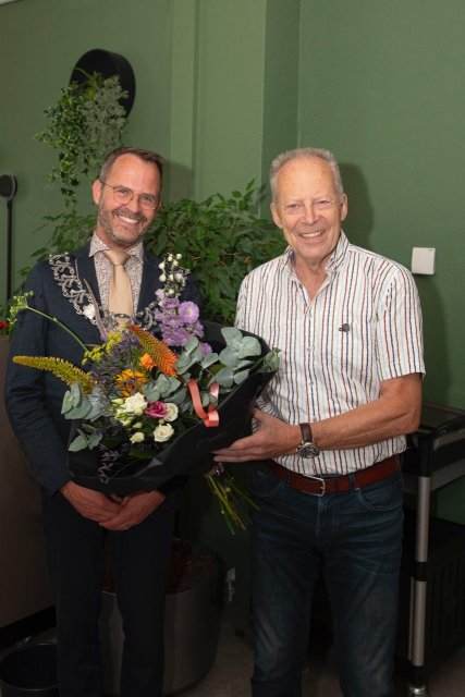 Burgemeester Laurens de Graaf en de heer Bas Stigter met de opgespelde gemeentelijke erespeld en bloemen