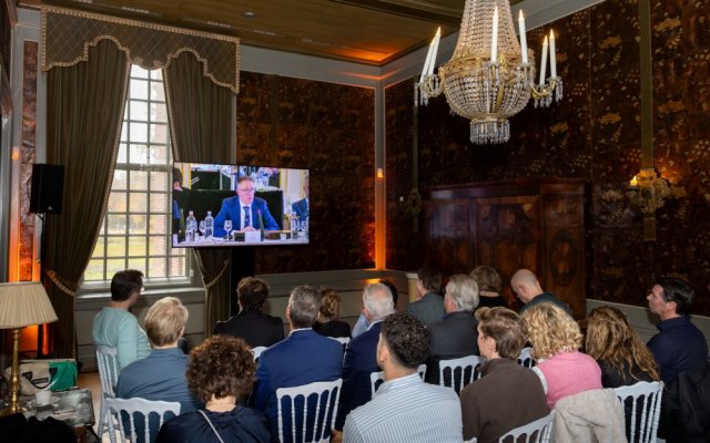 Toehoorders volgen de eerste vergadering via een tv-scherm