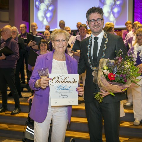 Locoburgemeester Martijn Kroonen reikt de Bokaal der Gemeente uit aan het Maassluise koor Sing for Joy tijdens het lustrumconcert op 22 november 2024. Het koor wordt geëerd voor haar 55 jaar lange inzet en betekenisvolle bijdrage aan het culturele leven van Maassluis.