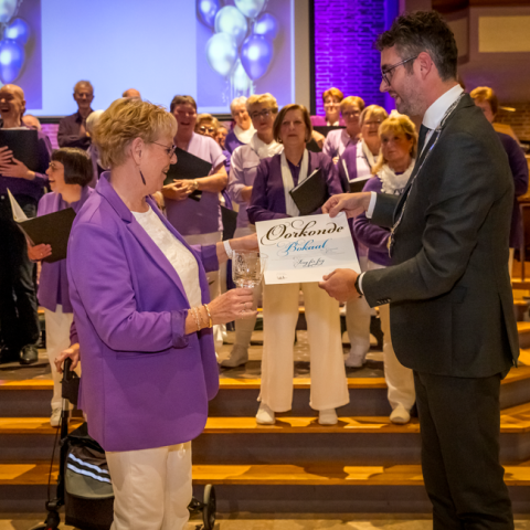 Locoburgemeester Martijn Kroonen reikt de Bokaal der Gemeente uit aan het Maassluise koor Sing for Joy tijdens het lustrumconcert op 22 november 2024. Het koor wordt geëerd voor haar 55 jaar lange inzet en betekenisvolle bijdrage aan het culturele leven van Maassluis.