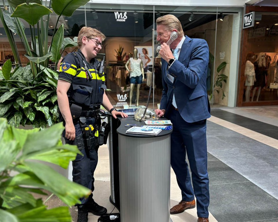 Burgemeester De Vries met de fraudefoon bij een politiestand