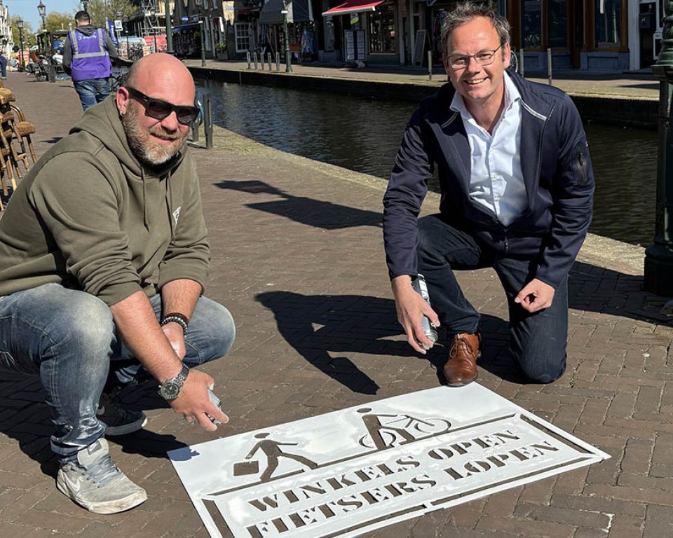 Thijs Boskamp en wethouder Kuiper spuiten de tekst 'Winkels open, fietsers lopen' op de straat