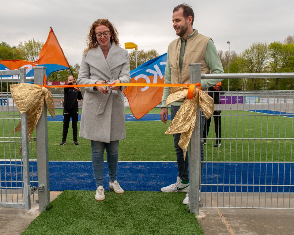 Wethouder Denise Mulder-Solleveld (links) knipte, onder toeziend oog van voorzitter Rick van Spronsen (rechts), het lint door bij de officiële opening van de vernieuwde kunstgrasvelden van c.k.c. Maassluis.  