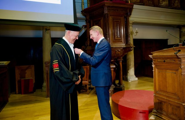 Op de afbeelding ziet u dat Dr. Peter van Baalen het lintje krijgt opgespeld van Jack de Vries, burgemeester van Maassluis