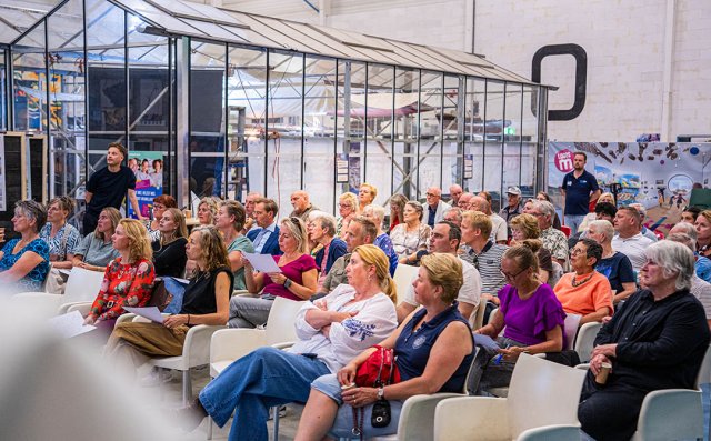 Foto van de de aanwezigen die luisteren naar de presentatie in Loods M 