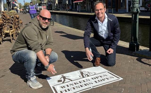 Thijs Boskamp en wethouder Kuiper spuiten de tekst 'Winkels open, fietsers lopen' op de straat