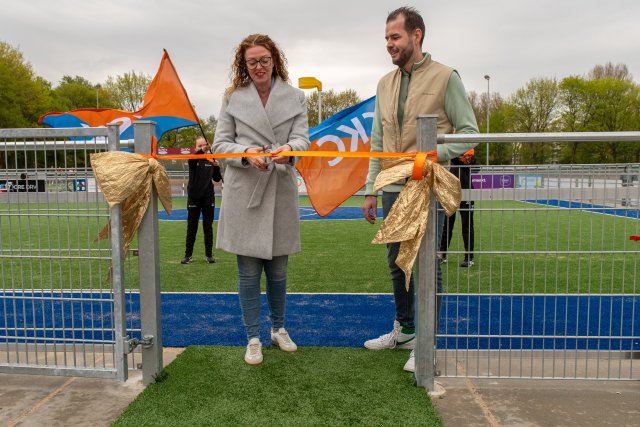Wethouder Denise Mulder-Solleveld (links) knipte, onder toeziend oog van voorzitter Rick van Spronsen (rechts), het lint door bij de officiële opening van de vernieuwde kunstgrasvelden van c.k.c. Maassluis.