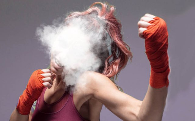 Een vrouwelijke vechtsporter die een vuist maakt tegen vapen met haar hoofd in de rook