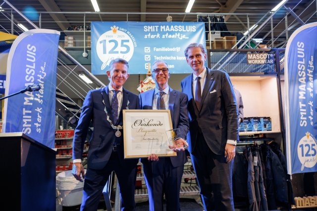 De foto toont dat burgemeester Jack de Vries de Marnix van Sint Aldegonde‑plaquette uitreikt aan Peter Smit, in het bijzijn van de Commissaris van de Koning in Zuid-Holland, als erkenning voor 125 jaar ondernemerschap en de bijzondere betekenis van Smit Maassluis voor de stad Maassluis.