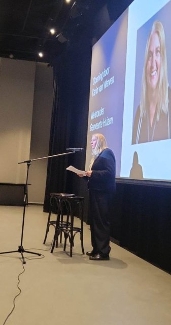 Wethouder Karin van Werven staat voor een presentatiescherm en spreekt naar de toehoorders in de zaal