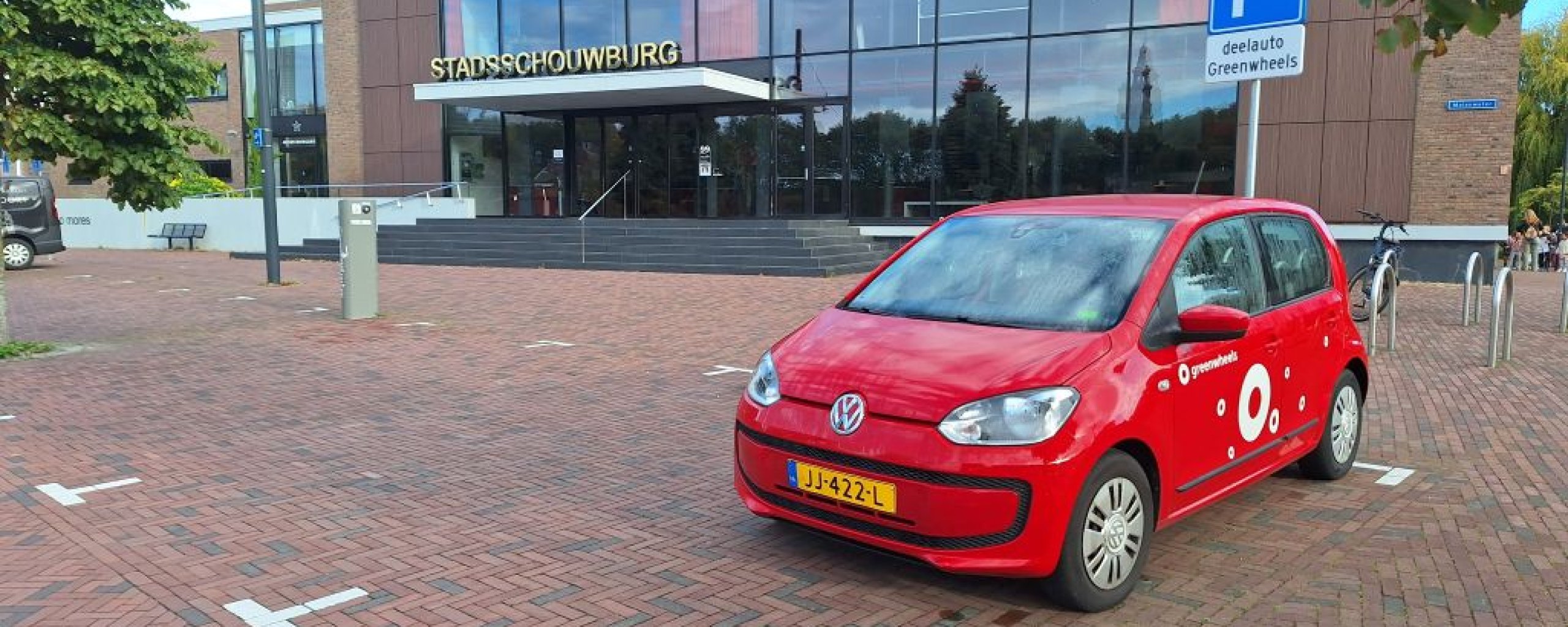 Rode auto van Greenwheels staat bij parkeerbord met tekst Deelauto Greenwheels