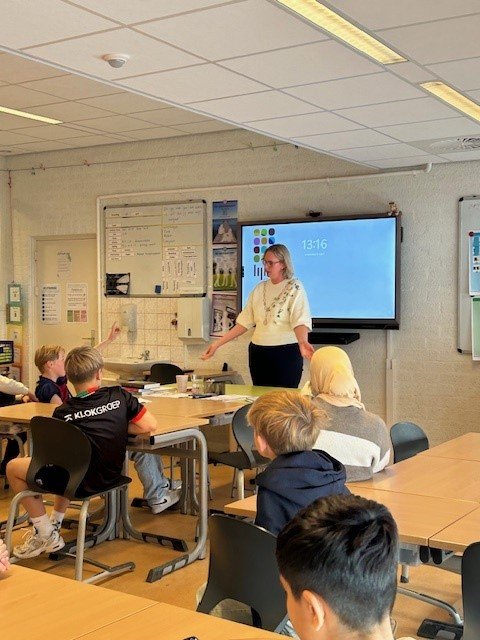 burgemeester van Dijk staat voor de klas en praat met een groep kinderen
