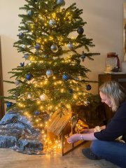 Burgemeester van Dijk zit op de grond voor de kerstboom om de kerststal in te richten.