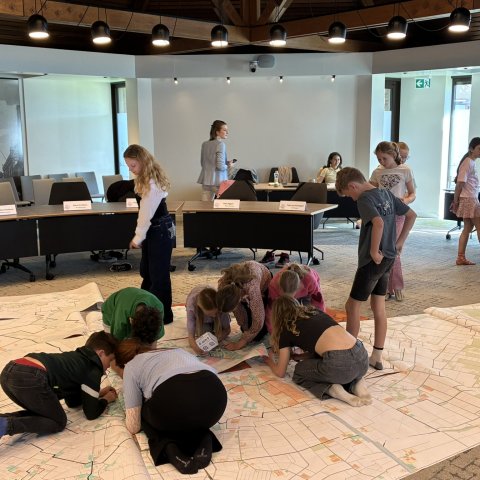 Leden van de kinderraad zoeken de locatie van hun basisschool op een grote plattegrond van Nederweert