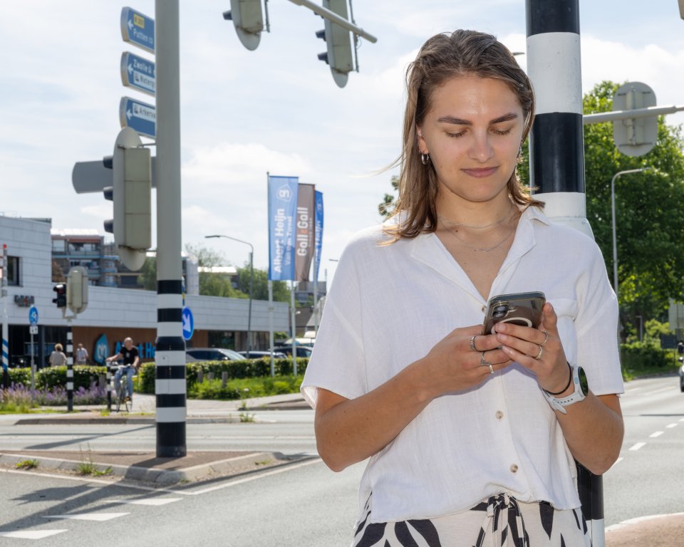 Vrouw kijkt op haar telefoon bij een kruispunt