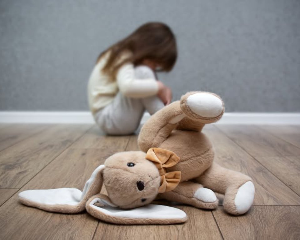 Kind ineen gehurkt met knuffel op de voorgrond