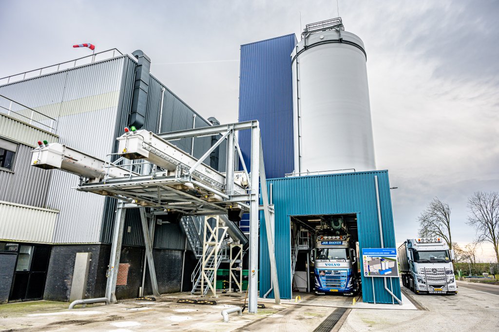 Een foto van de buitenzijde van de slibverwerkingsinstallatie, met twee transporttrucks