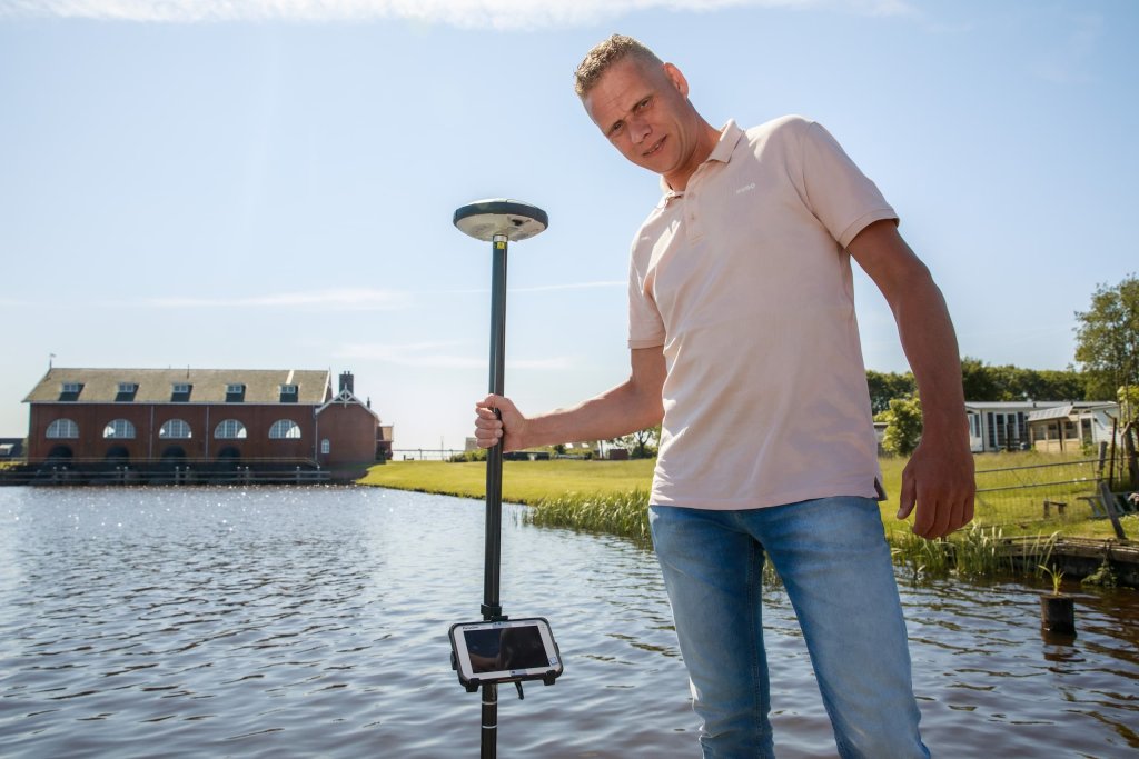 Roelf staat voor gemaal De Waterwolf met een peilstok in zijn hand