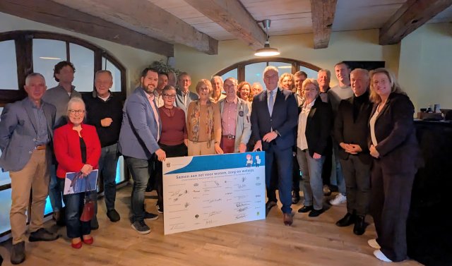 Bord met handtekeningen en daaromheen alle ondertekenaars van het uitvoeringsprogramma Woonzorgvisie