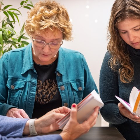 Drie personen bladeren in het boekje.