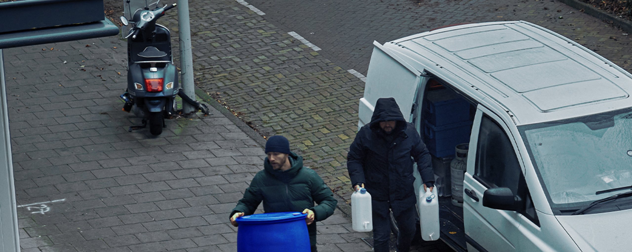 Twee mannen dragen containers van hun busje naar een drugslab. 