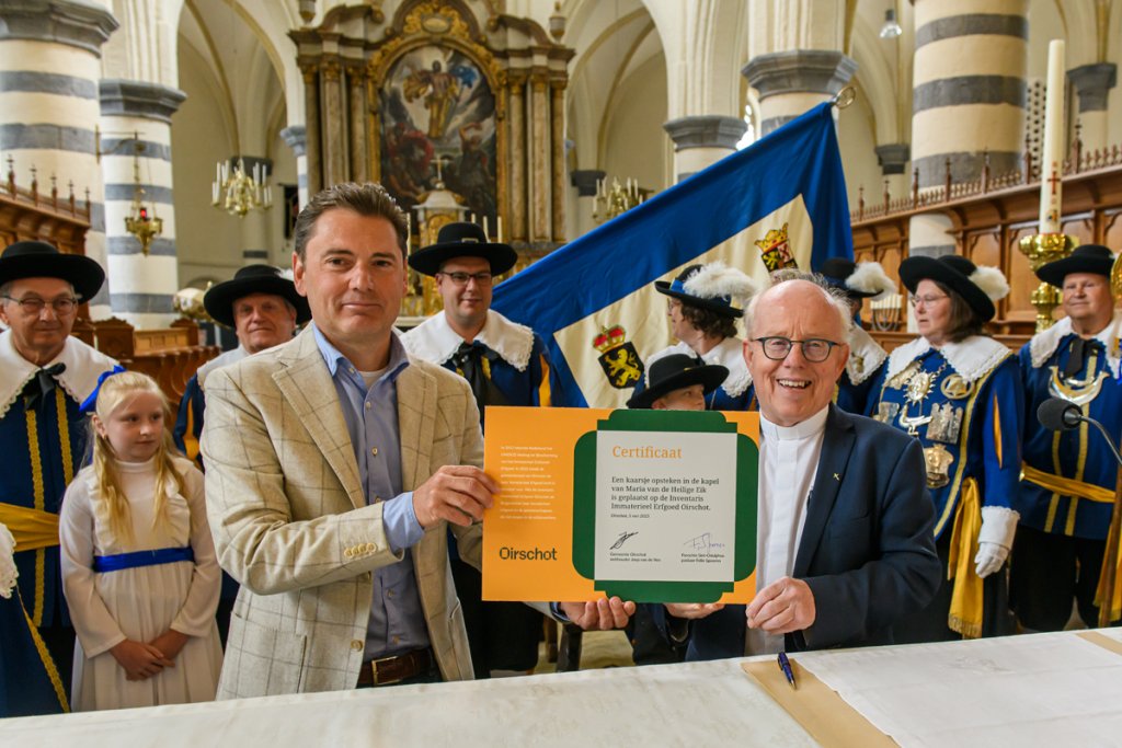 Wethouder Joep van de Ven en pastoor Felie Spooren tekenen het certificaat waarmee de traditie van het ‘kaarsje aansteken bij Maria van de Heilige Eik’ tot immaterieel erfgoed van Oirschot wordt verklaard.