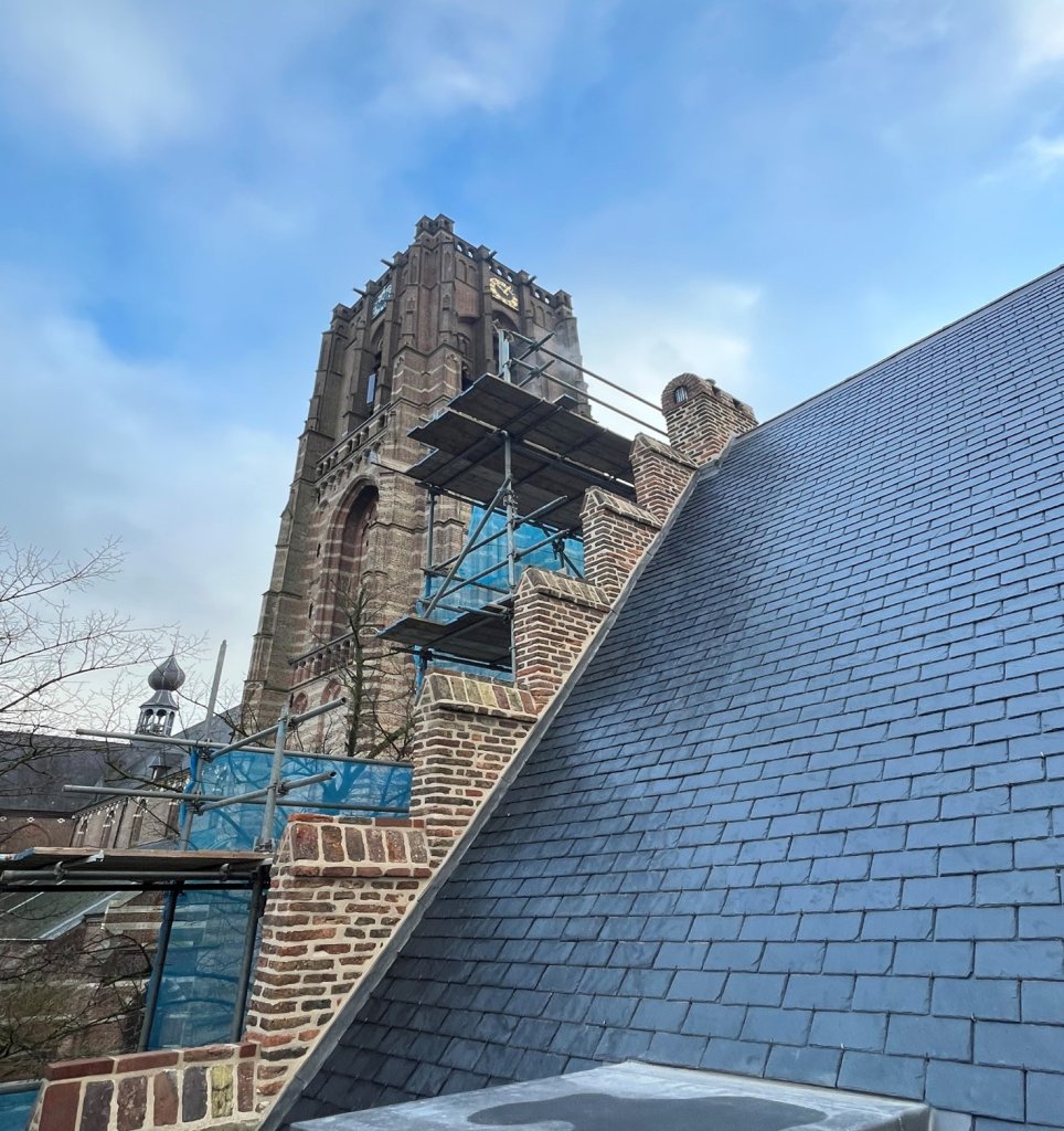 Het gerestaureerde dak van het Oude Raadhuis te Oirschot aan de linker achterzijde met trapgevel,           ezelsruggen en schoorsteen met op de achtergrond de toren van de Sint-Petrusbasiliek.